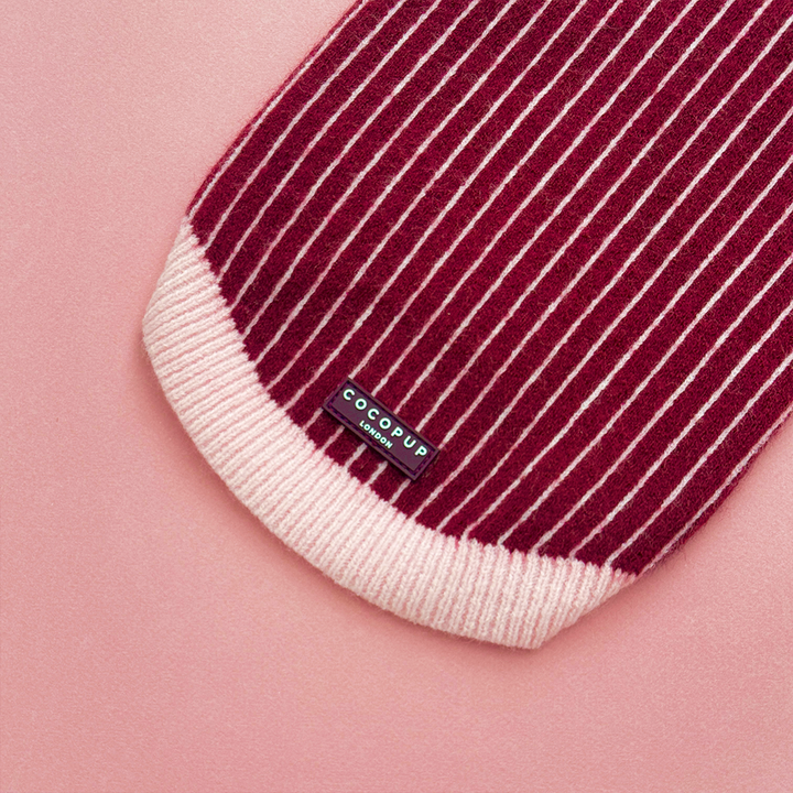 Close up of knitted dog jumper in burgundy with thin baby pink vertical stripes, featuring a pink collar with scalloped edging.