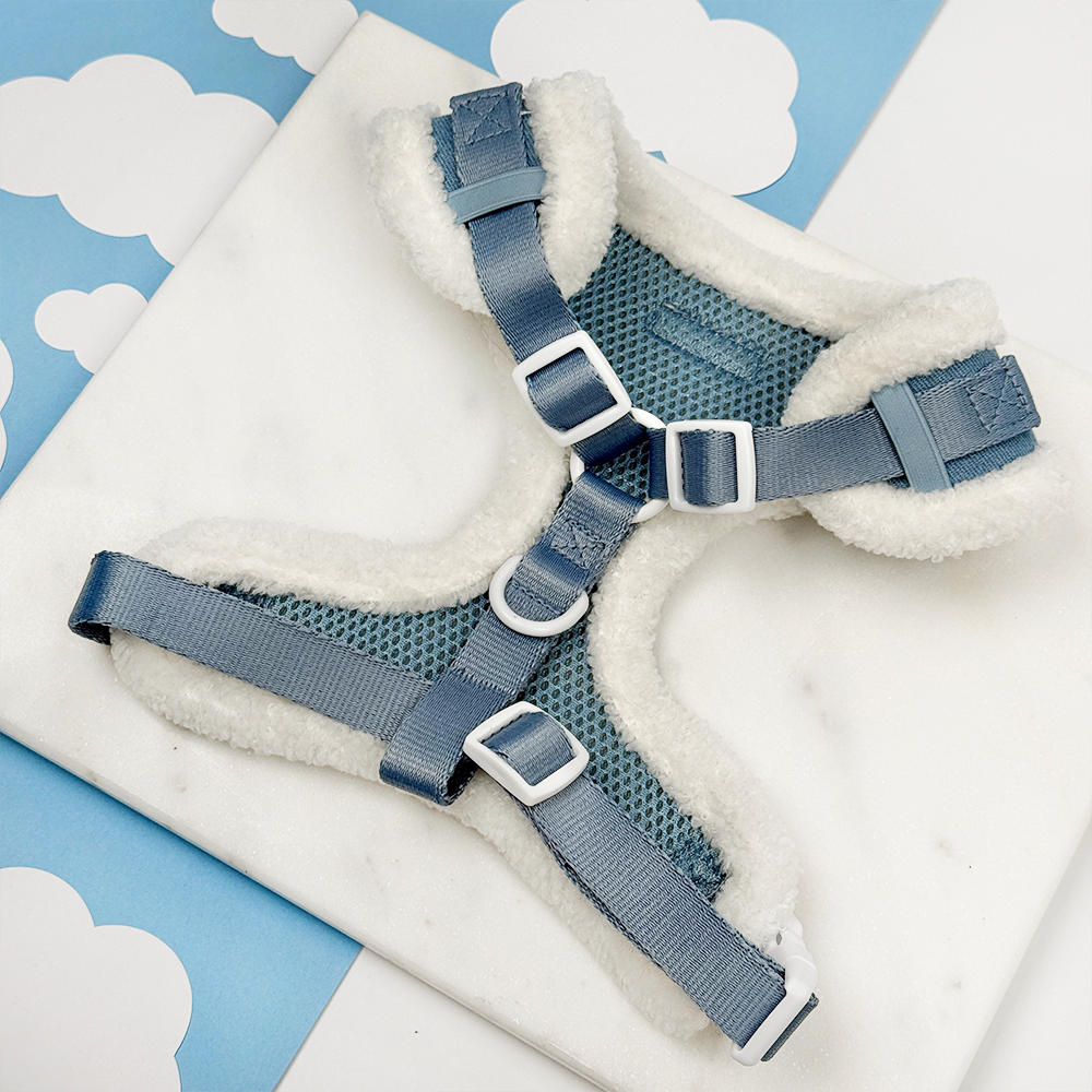 Blue dog harness with white fleece lining on a blue and white cloud-patterned background