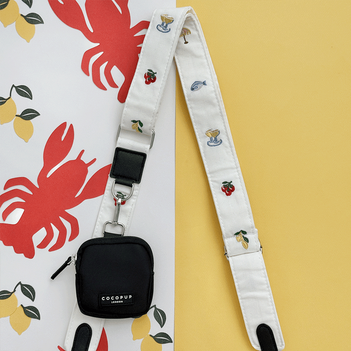 White linen fabric Bag Strap with summer embroidered embellishments. Attached to a black Cocopup Treat Pouch.