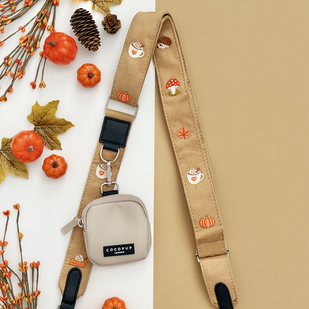 Brown bag strap, with attached treat pouch, with autumnal-themed embroidery of pumpkins, leaves, a coffee cup, and mushrooms.
